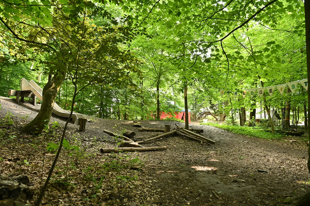 Spielplatz der Kinderkreisel-Kita Waldgeistergruppe mit Rutsche und Baumstämmen zum Balancieren.