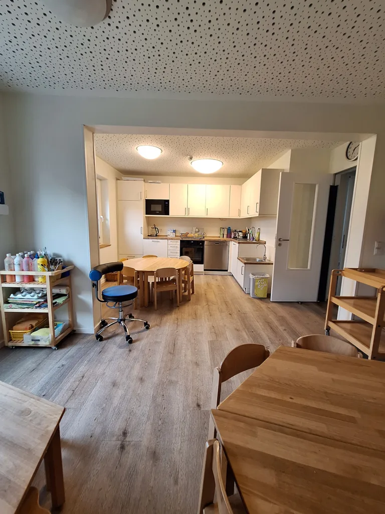 Essbereich der Kinderkreisel Kita mit Küche, kindgerechten Tischen und Malmaterial im Regal