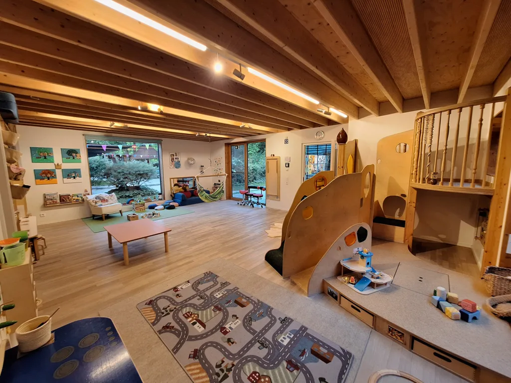 Gruppenraum der Kinderkreisel-Kita Mäusegruppe mit Kletterburg, Spielteppich, Hängematte, Sitzmöglichkeiten und Regalen zur Aufbewahrung von Spielzeug und Materialien für verschiedene Aktivitäten.
