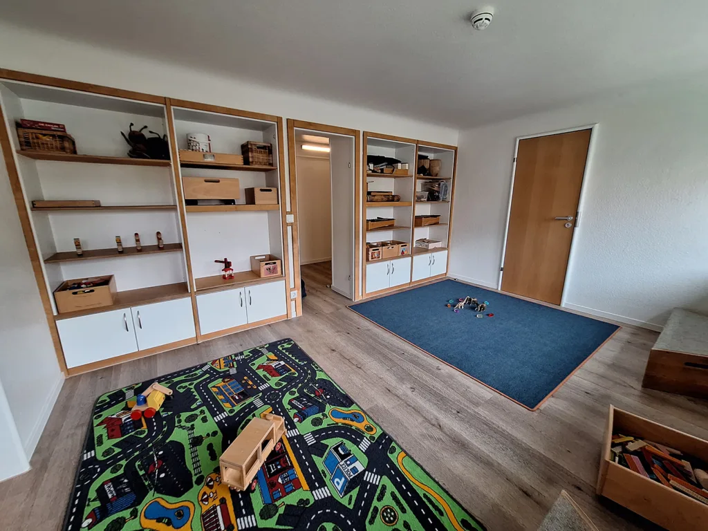 Spielraum der Kinderkreisel-Kita Drachengruppe mit viel Stauraum durch Regale mit Boxen sowie Teppichen auf dem Boden zum Spielen.