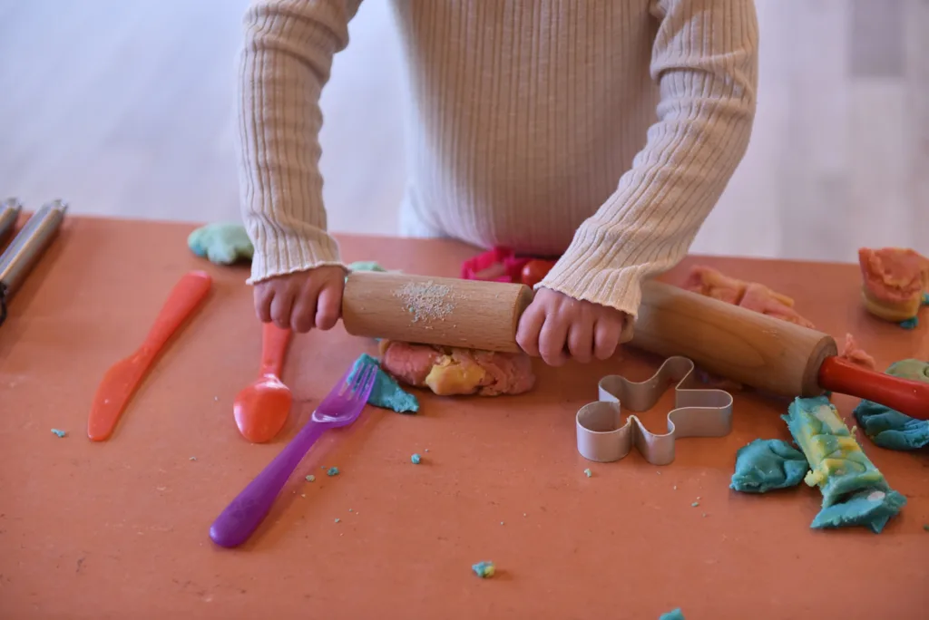 Kleinkind formt Knete mit Teigroller und Werkzeugen zur Förderung der Feinmotorik.