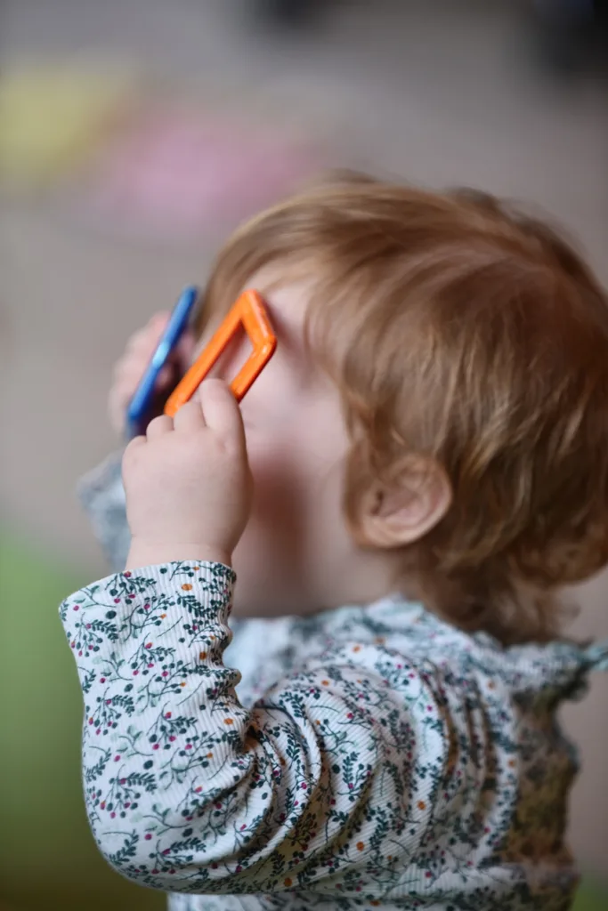 Kleinkind spielt mit Holzformen und hält sie vor die Augen, um hindurchzuschauen.
