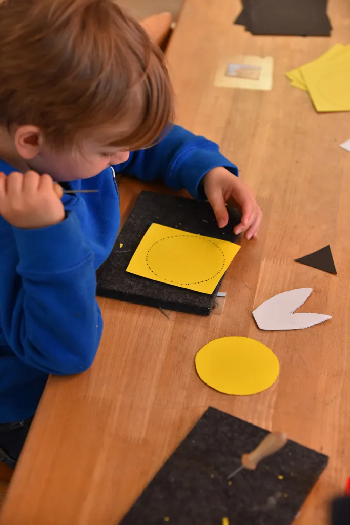 Kleinkind schneidet Formen aus Papier, indem es entlang der Konturen Löcher in das Papier sticht.