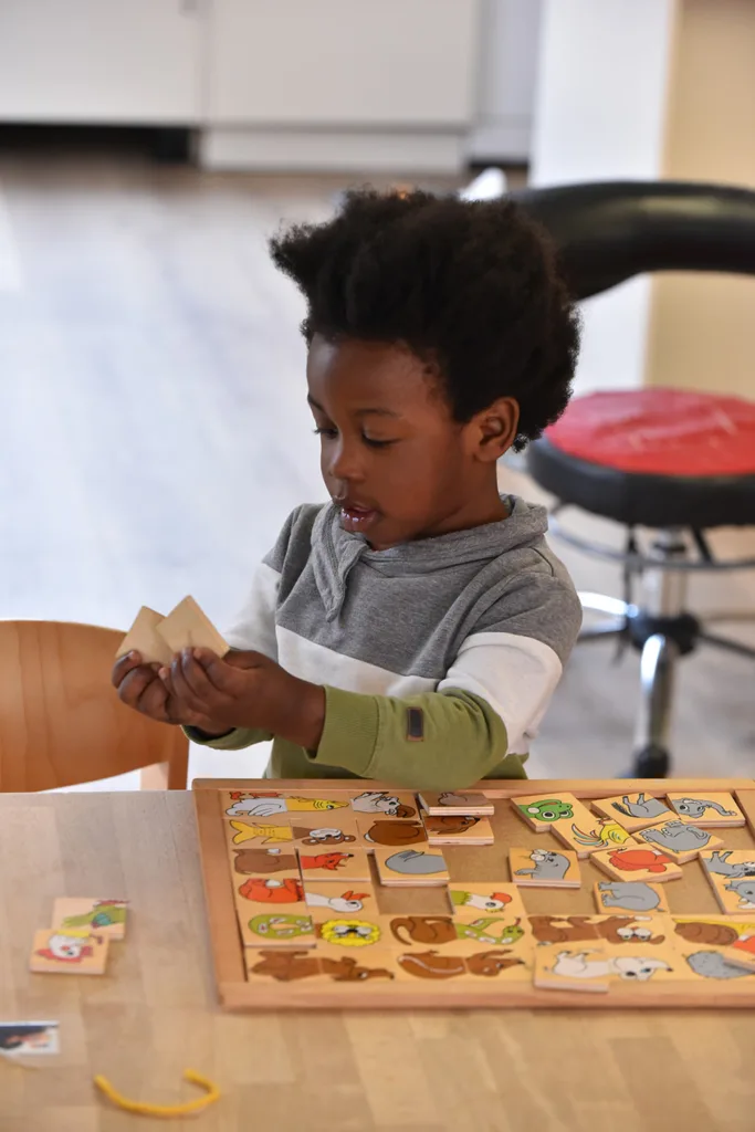Kleinkind legt ein Holzpuzzle mit verschiedenen Tieren zusammen und fördert spielerisch die Feinmotorik.