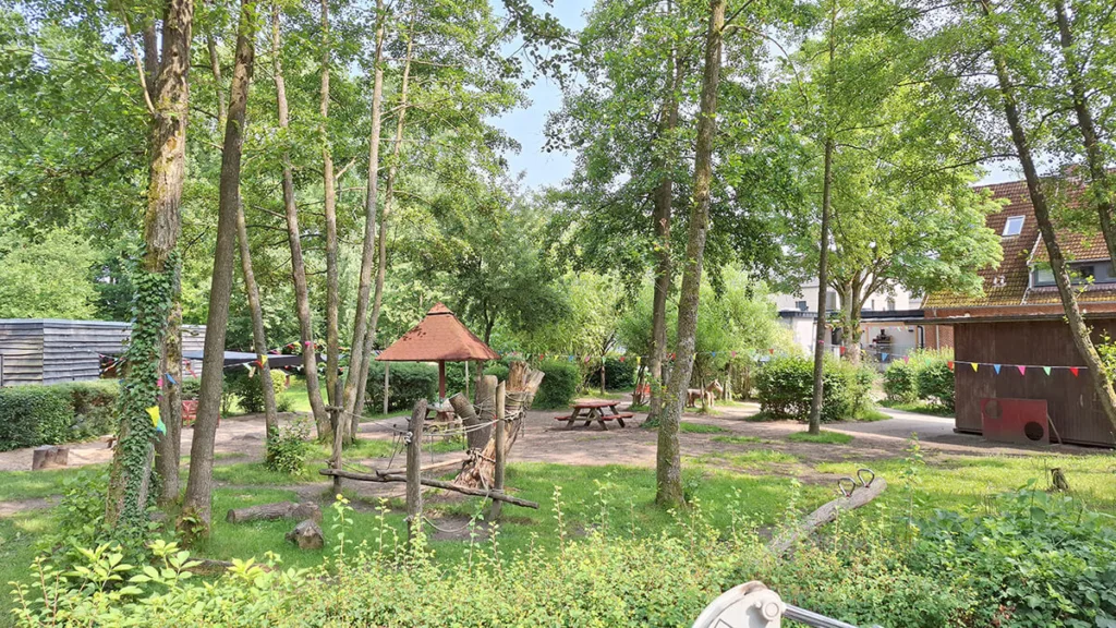 Spielplatz der Kinderkreisel-Kita mit Balanciergerüst, Wippe und Sitzbereich.